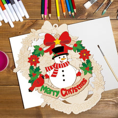 Christmas-themed wooden cutout with a snowman, wreath, and 'Merry Christmas' text on a wooden surface with coloring supplies.
