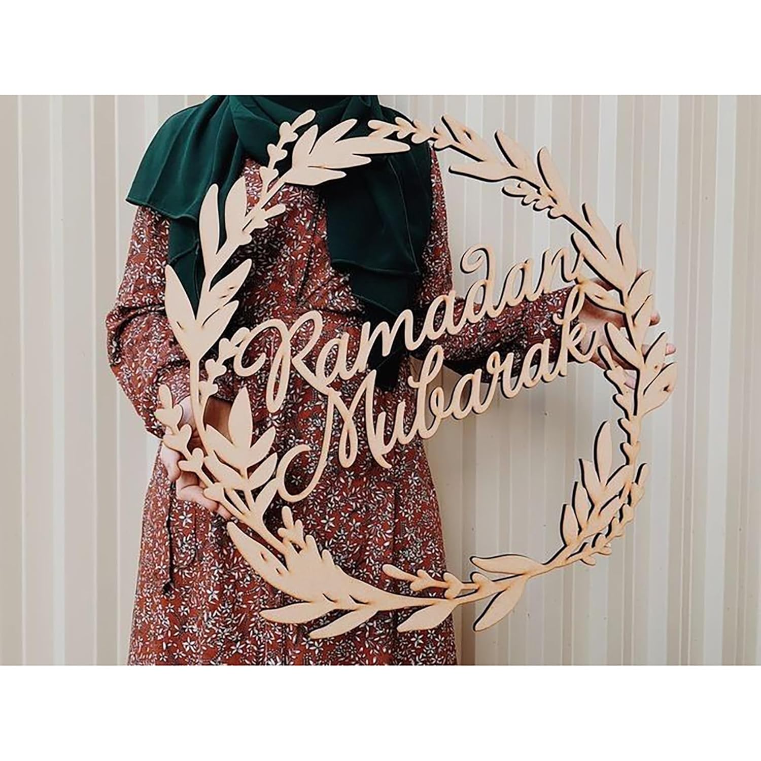 Decorative wreath with 'Ramadan Mubarak' text in front of a person wearing a green headscarf and patterned dress.