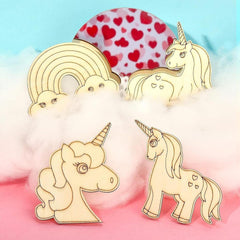 Set of unicorn and rainbow-shaped wooden pins on a colorful background with heart pattern.