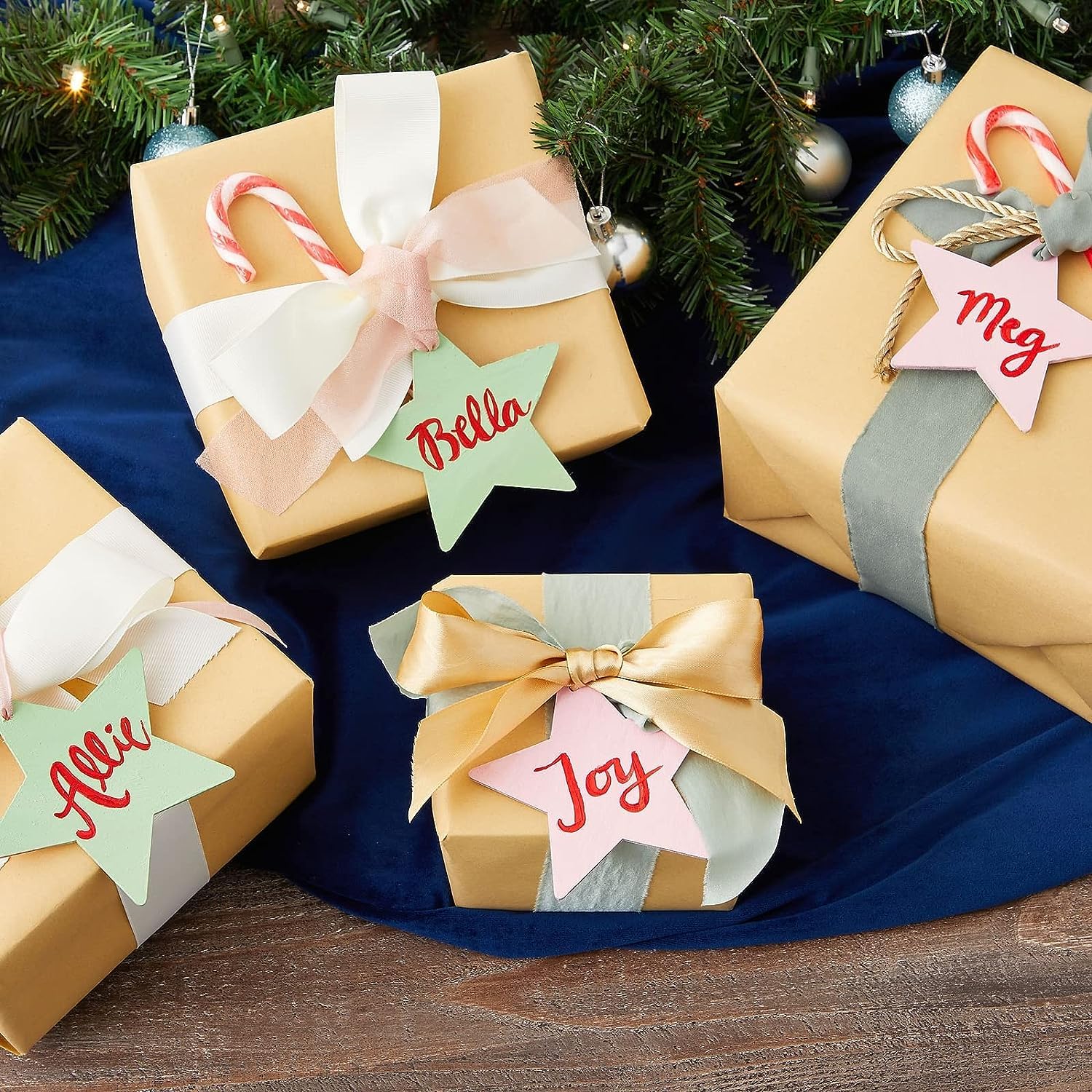 Gift boxes wrapped in gold paper with decorative ribbons and name tags under a Christmas tree.
