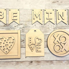 Wooden decorative items including a 'Be Mine' banner, heart-shaped tags, and a 'XO OX' design on a wooden surface.