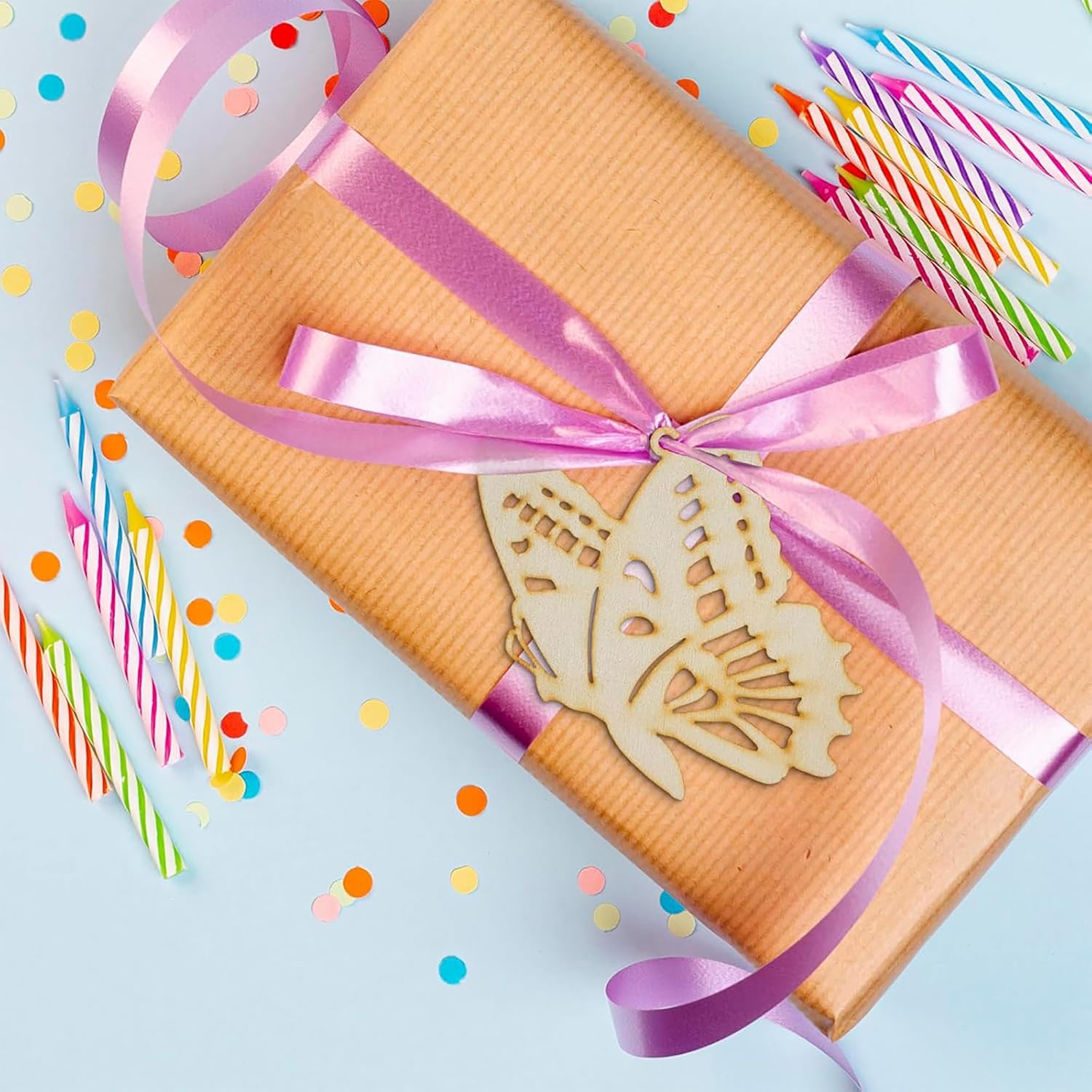 Gift box with pink ribbon and butterfly decoration, surrounded by colorful candles and confetti on a light blue background