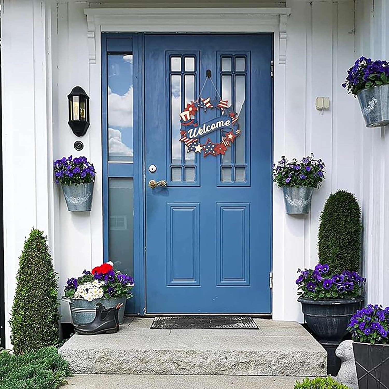 Blue front door with decorative wreath and potted plants on a white house.