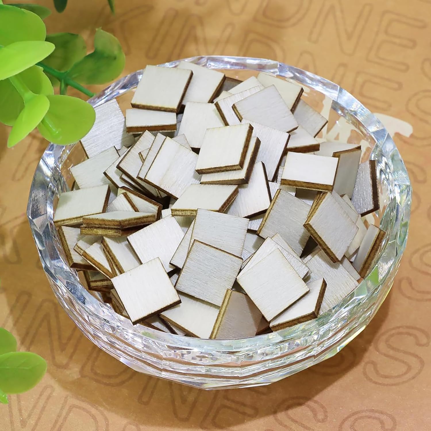 Small square tiles with gold accents in a clear glass bowl on a patterned surface.