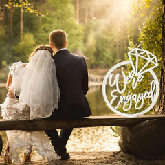 Couple sitting on a log by a lake with 'We're Engaged' sign overlay