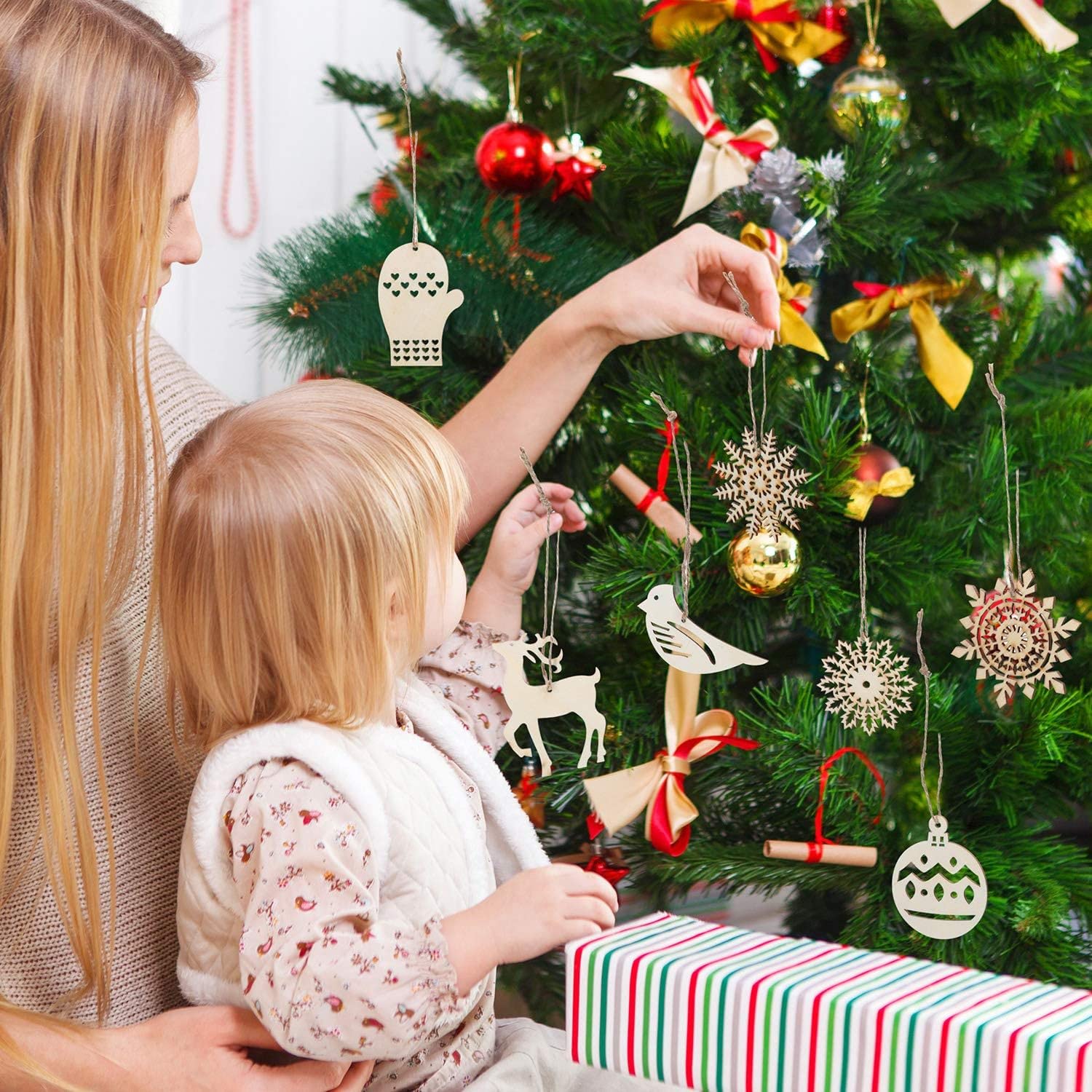 Woman and child decorating a Christmas tree with ornaments and a present underneath.