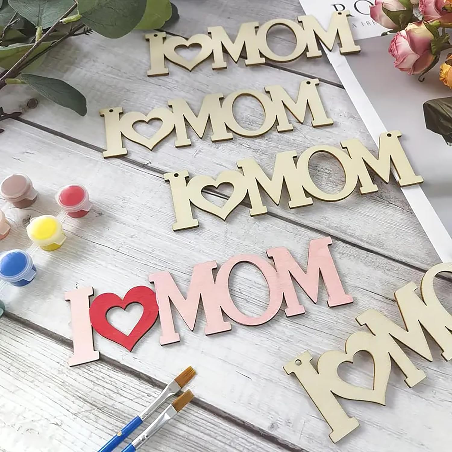 Wooden letters spelling 'I ❤️ MOM' on a wooden surface with paint bottles and brushes.