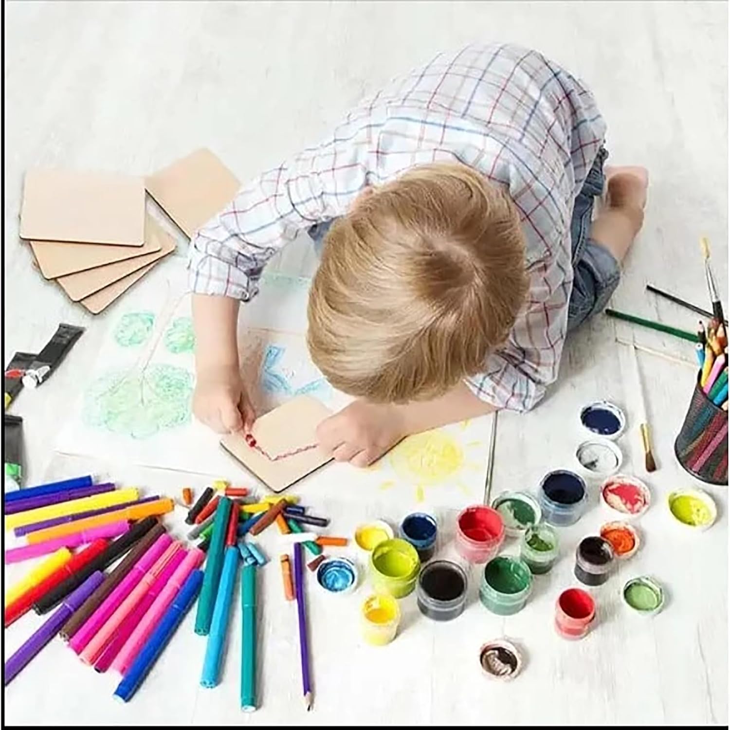 Child engaged in art activities with markers, paint, and paper on a white surface