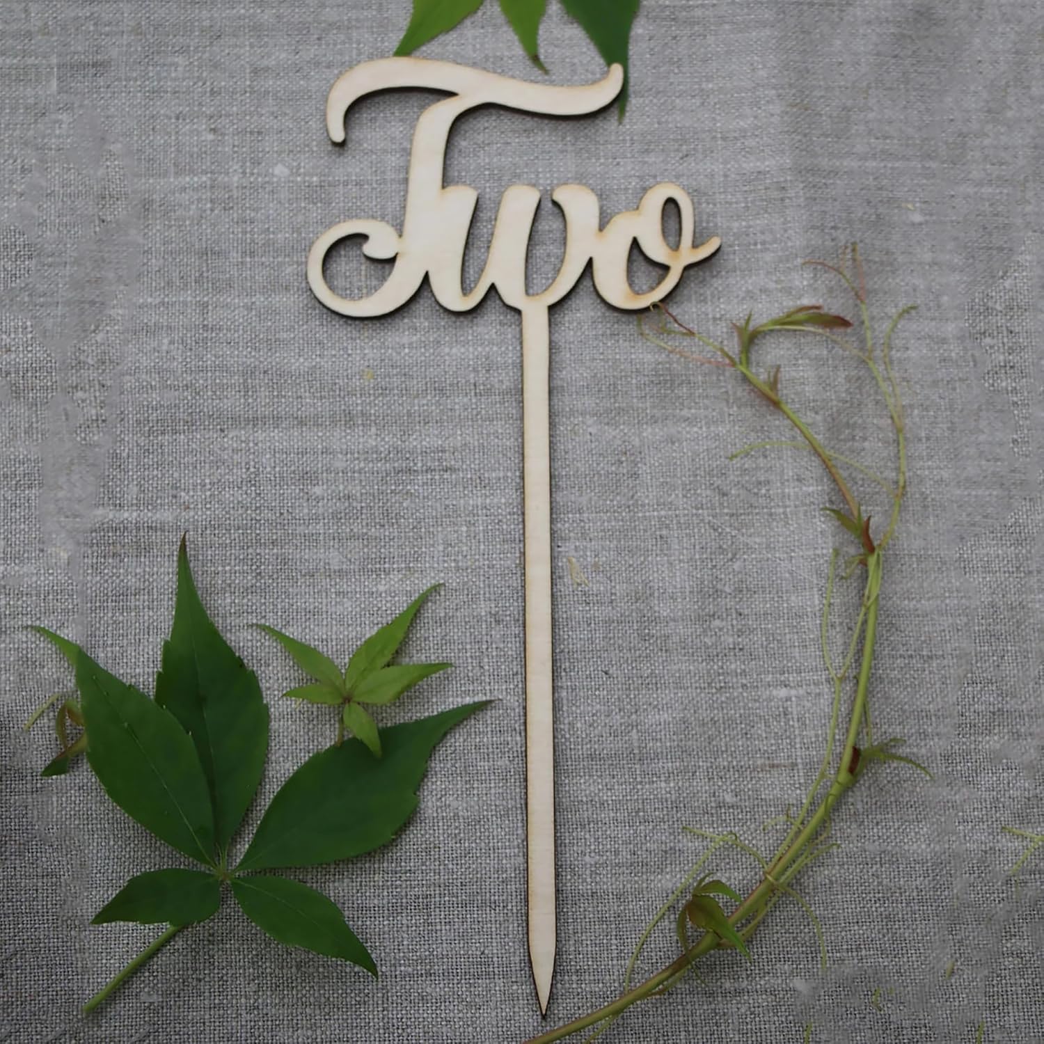 Wooden 'Two' cake topper with green leaves on a gray fabric background
