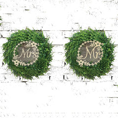 Two green wreaths with 'Mr.' and 'Mrs.' signs on a white brick wall.