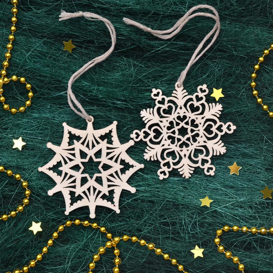 Decorative snowflake ornaments on a textured green surface with gold beads and stars.