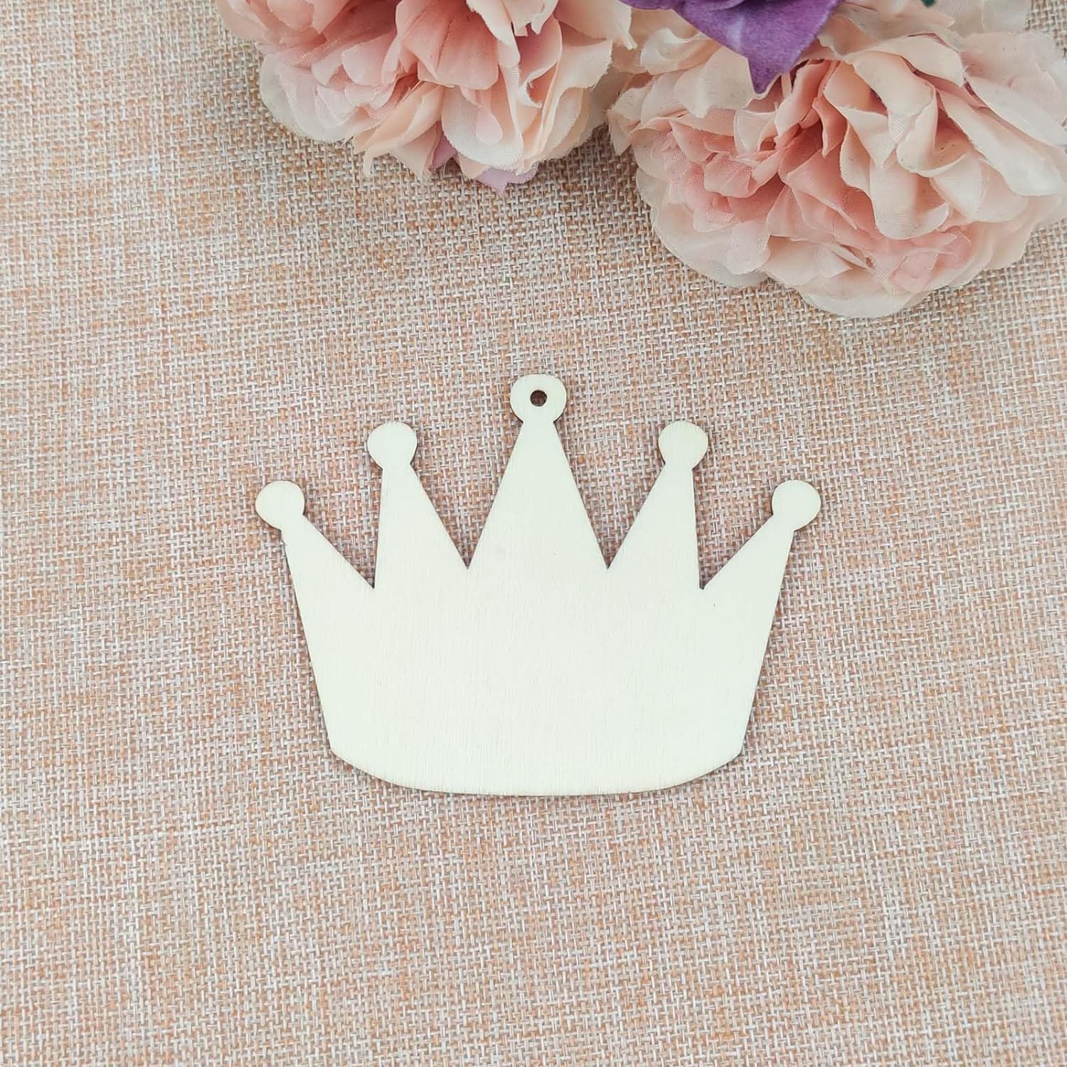 White crown-shaped object on a textured beige surface with pink flowers in the background