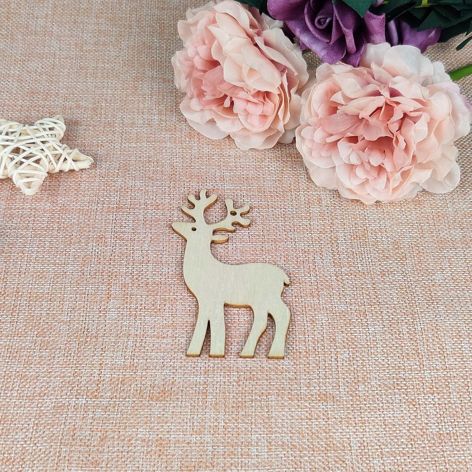 Wooden deer ornament on a textured surface with pink flowers in the background