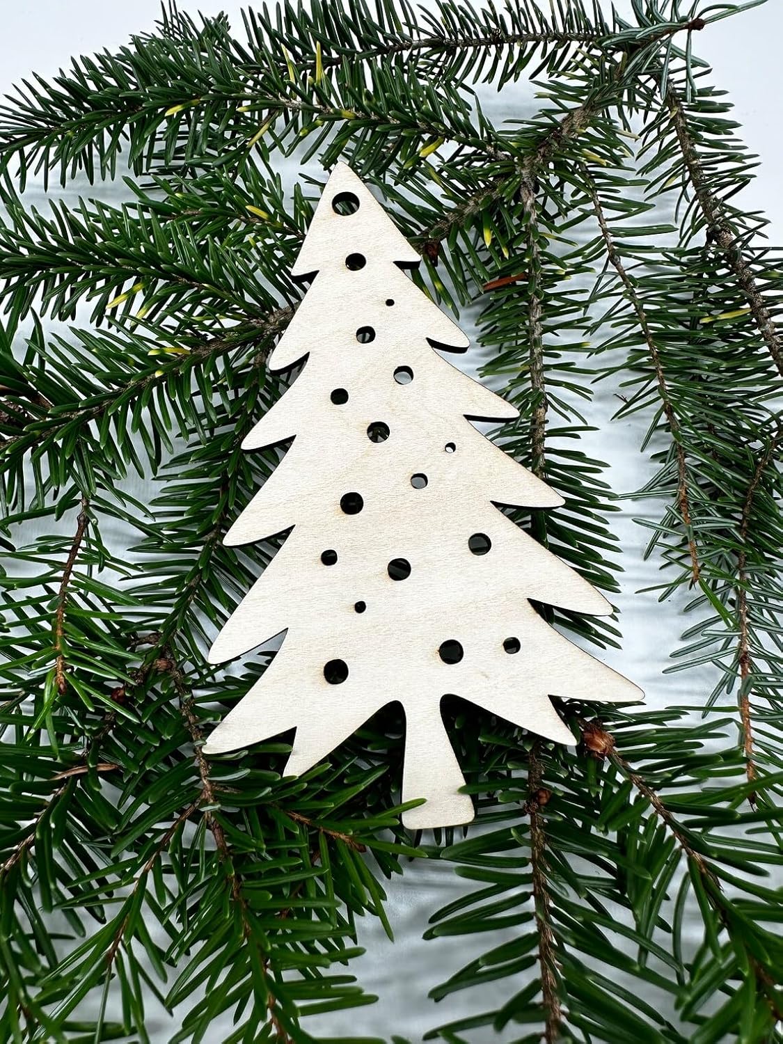 White Christmas tree ornament with black dots on a green pine branch