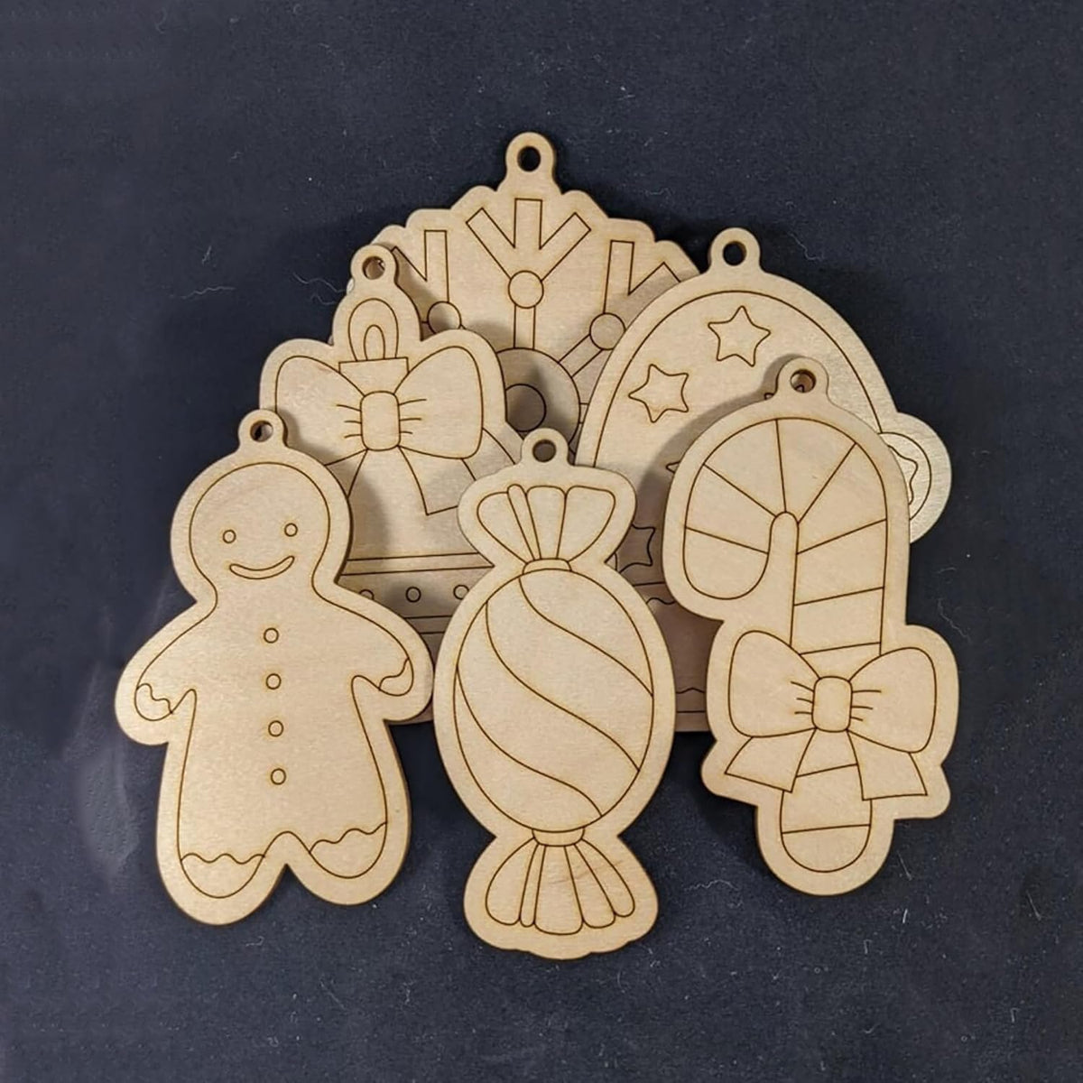 Wooden Christmas ornaments shaped like gingerbread man, candy, and bow on a dark background