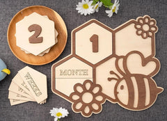 Wooden baby milestone cards with numbers and a bee design on a textured surface.