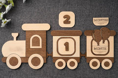 Wooden train-themed baby milestone cards with numbers and 'month' markers on a textured surface.
