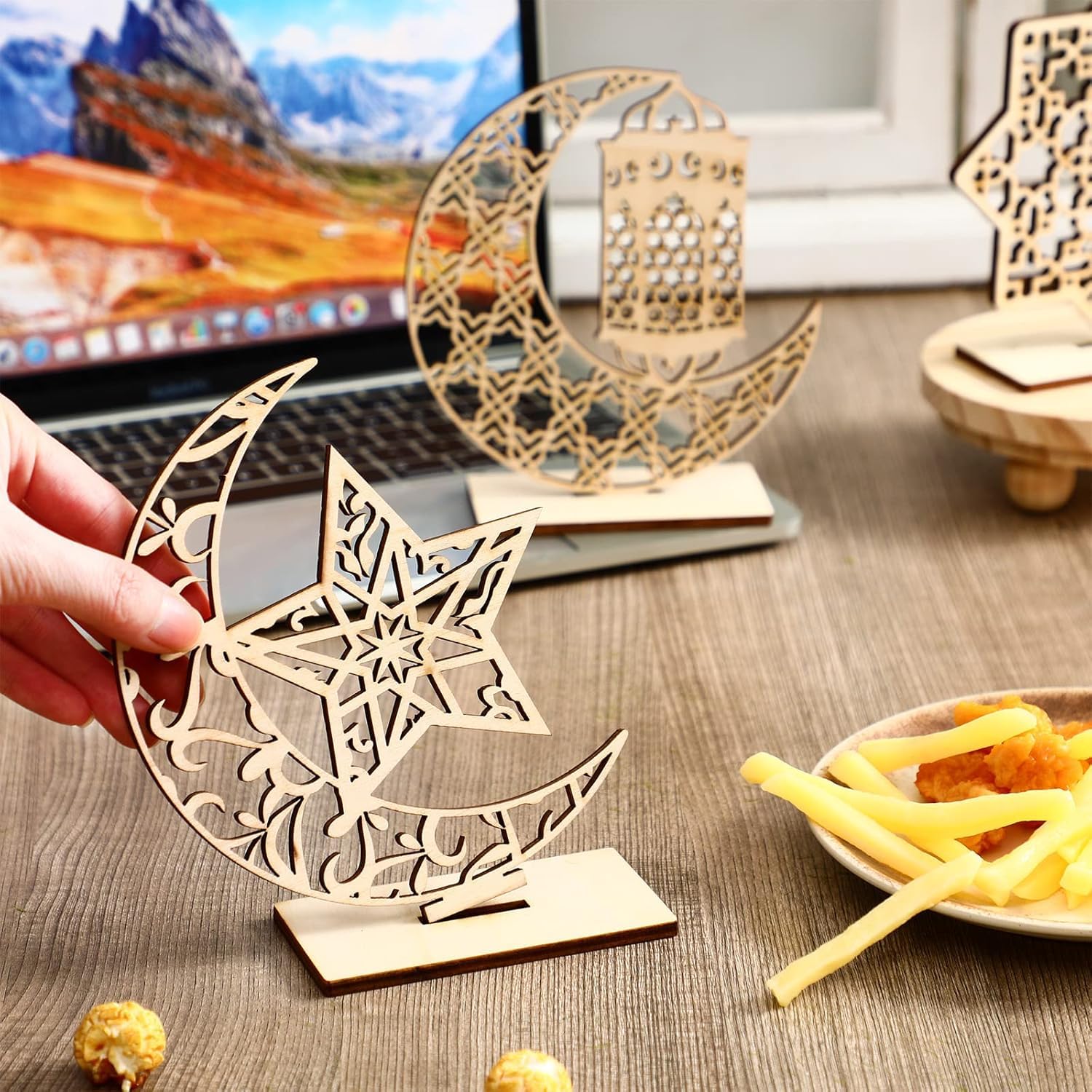 Wooden star and crescent moon decoration on a desk with a laptop and snacks.