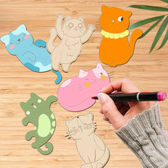 Colorful cat-shaped paper cutouts on a wooden surface with a hand holding a marker.