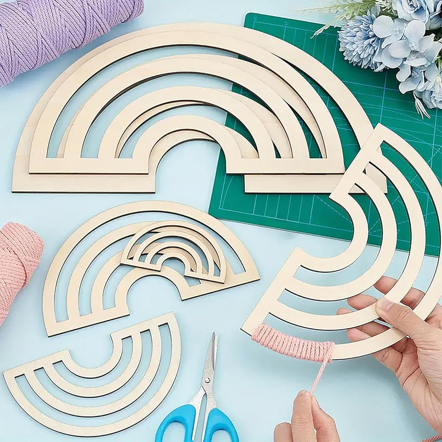 Wooden rainbow shapes with hands working on a craft project on a light blue surface.
