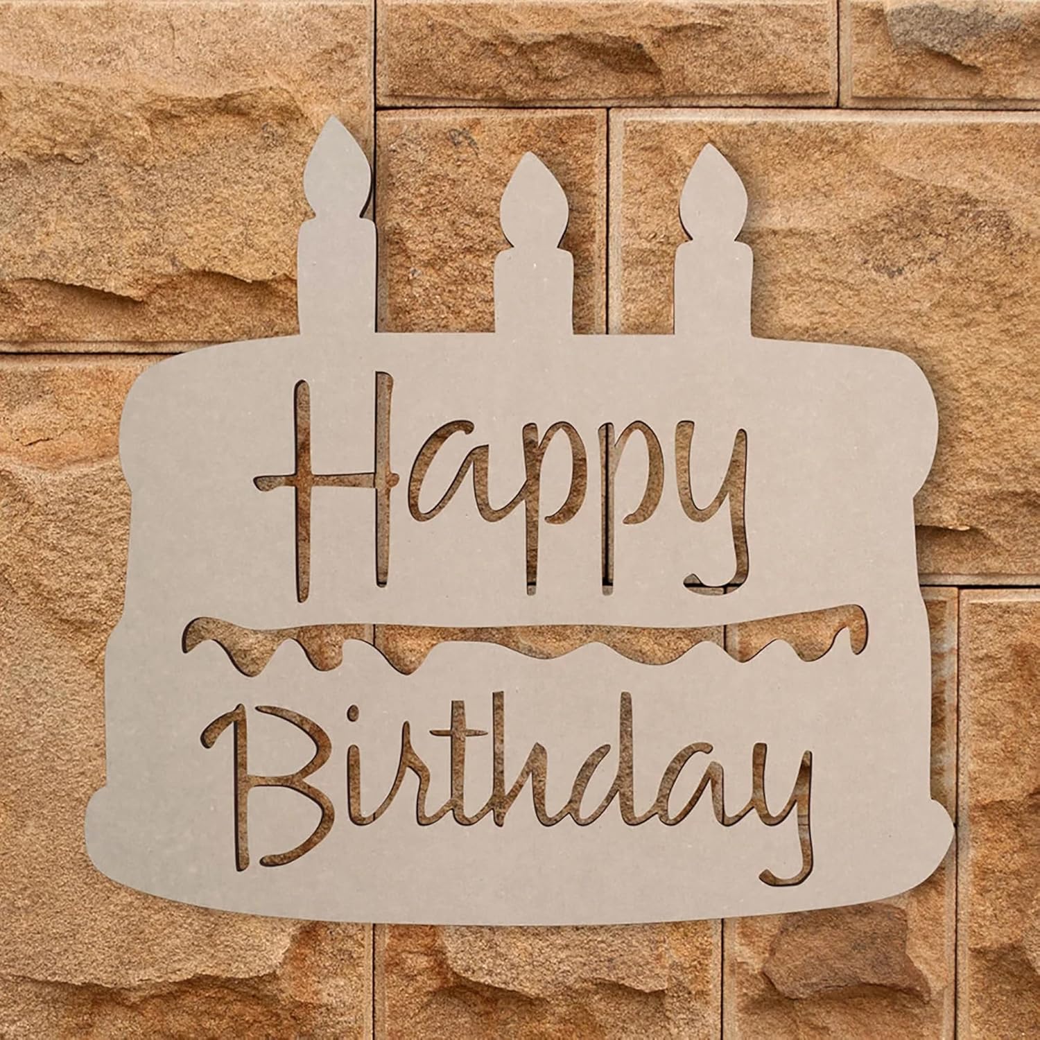 Decorative sign shaped like a birthday cake with 'Happy Birthday' text on a stone wall background
