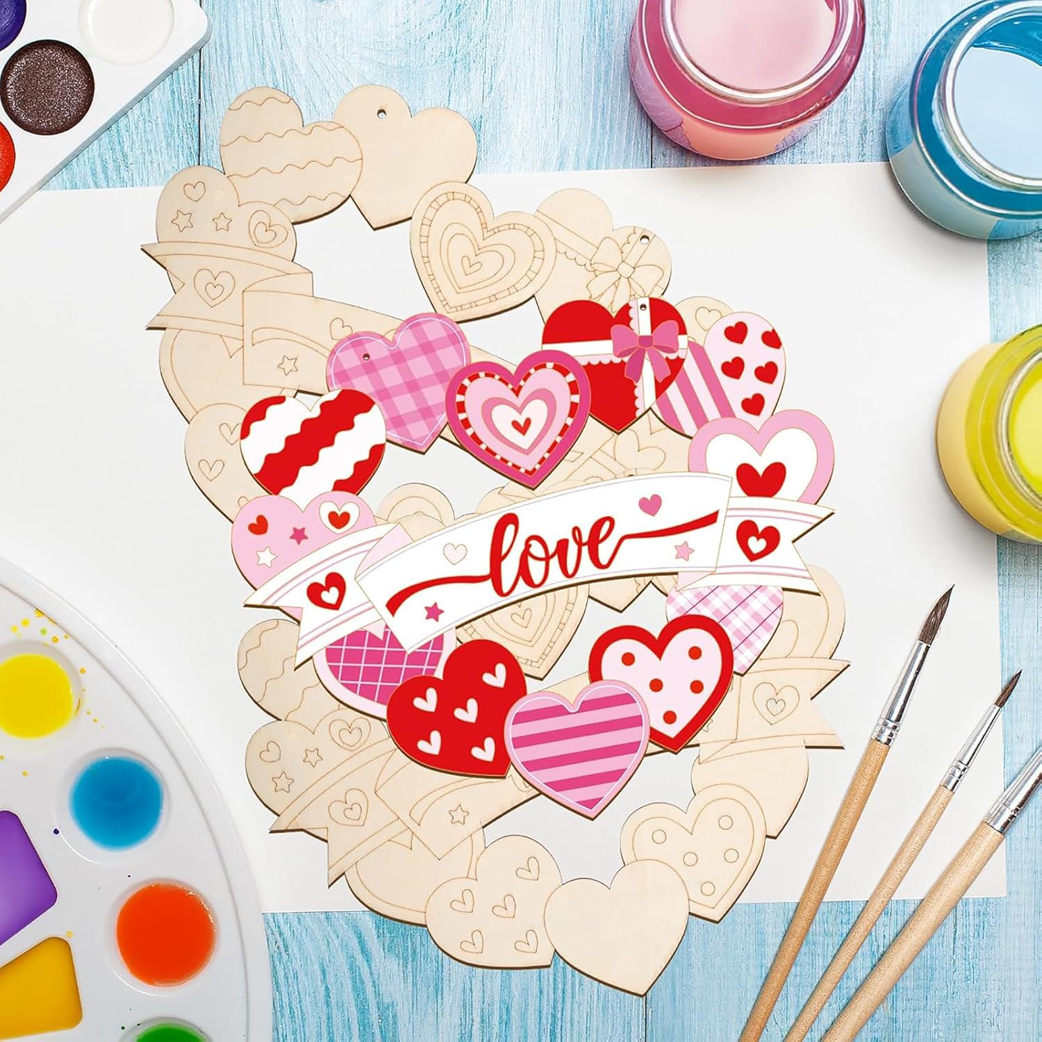 Heart-shaped wooden craft pieces with paint and brushes on a blue surface