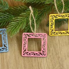 Decorative square frames in pink, yellow, and blue hanging on a wooden surface with greenery.
