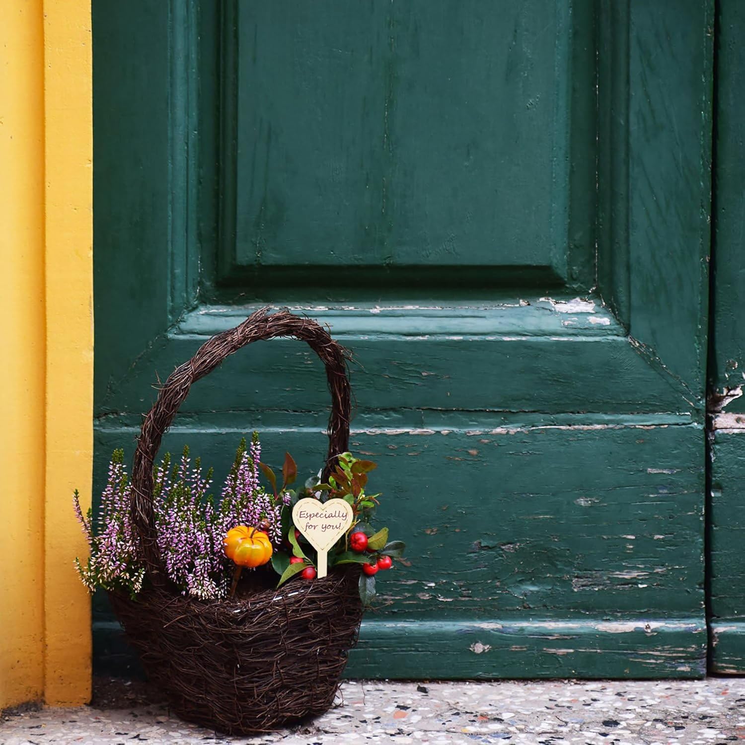 Wicker basket with flowers and a heart-shaped sign against a green door.