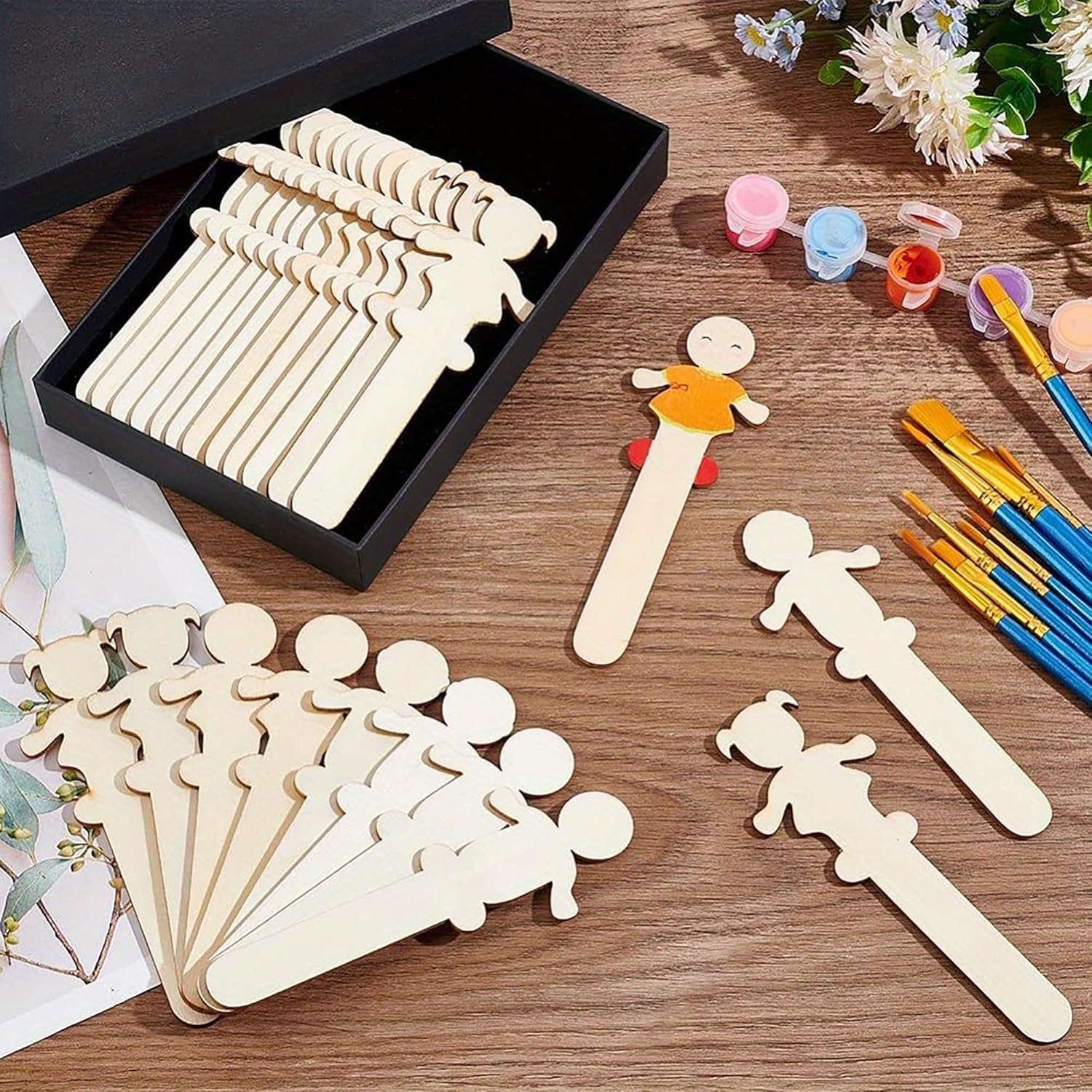 Wooden cutouts of people on sticks with painting supplies on a wooden surface