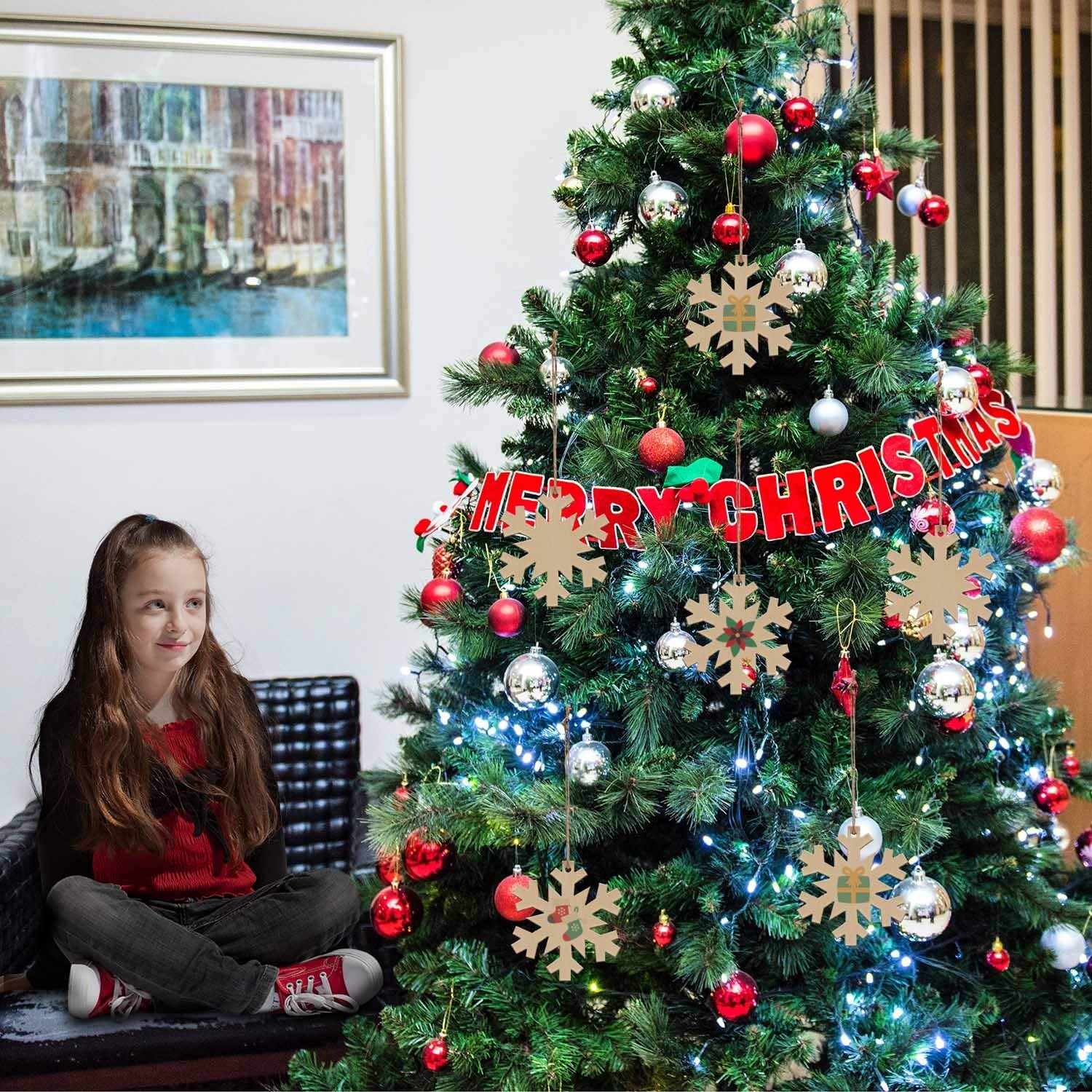 Child sitting next to a decorated Christmas tree with 'Merry Christmas' sign.