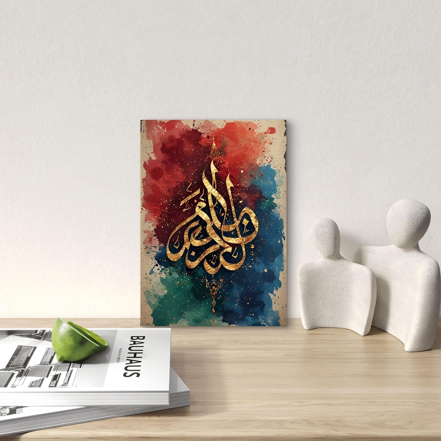Decorative wall art with calligraphy on a colorful abstract background, placed on a wooden surface with books and sculptures.