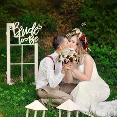 Couple in a romantic setting with 'Bride to Be' sign and floral decorations.