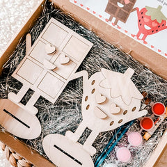 Wooden craft items and paint cans in a box with straw bedding