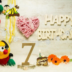 Birthday decoration with cake, number '7', and 'Happy Birthday' sign on a wooden surface.