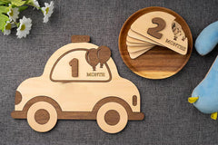 Wooden baby milestone cards with car and flower decorations on a textured surface
