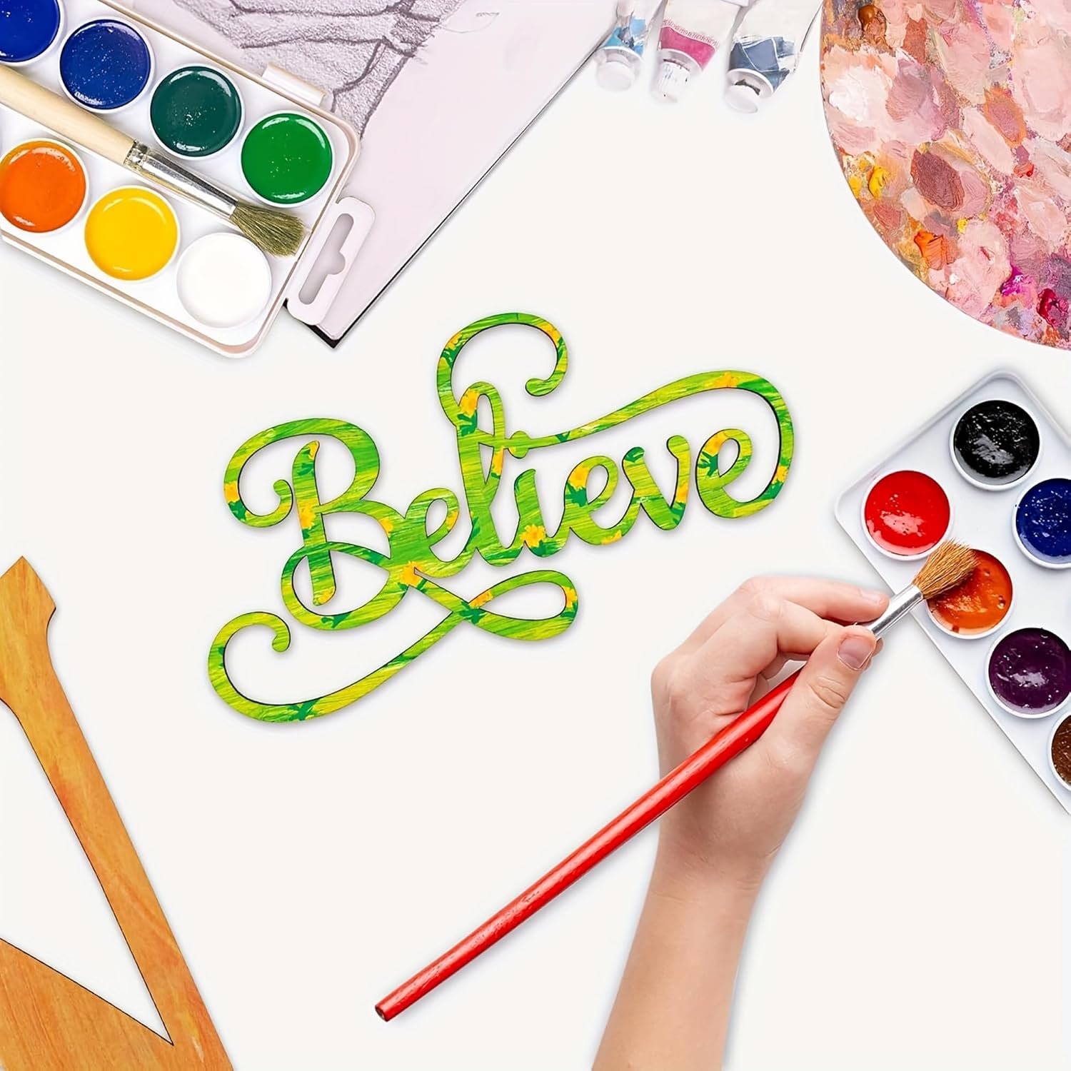 Colorful 'Believe' text being painted with watercolor paints on a white surface.