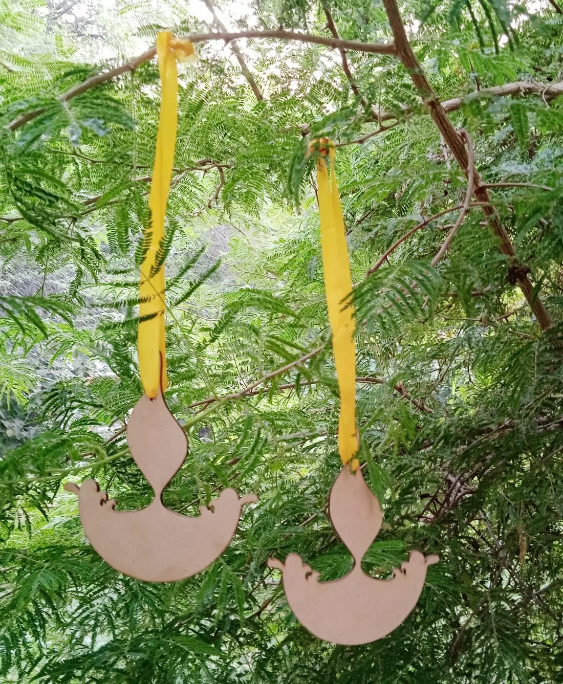 Decorative metal ornaments shaped like spoons and ladles hanging from yellow ribbons against a green leafy background.