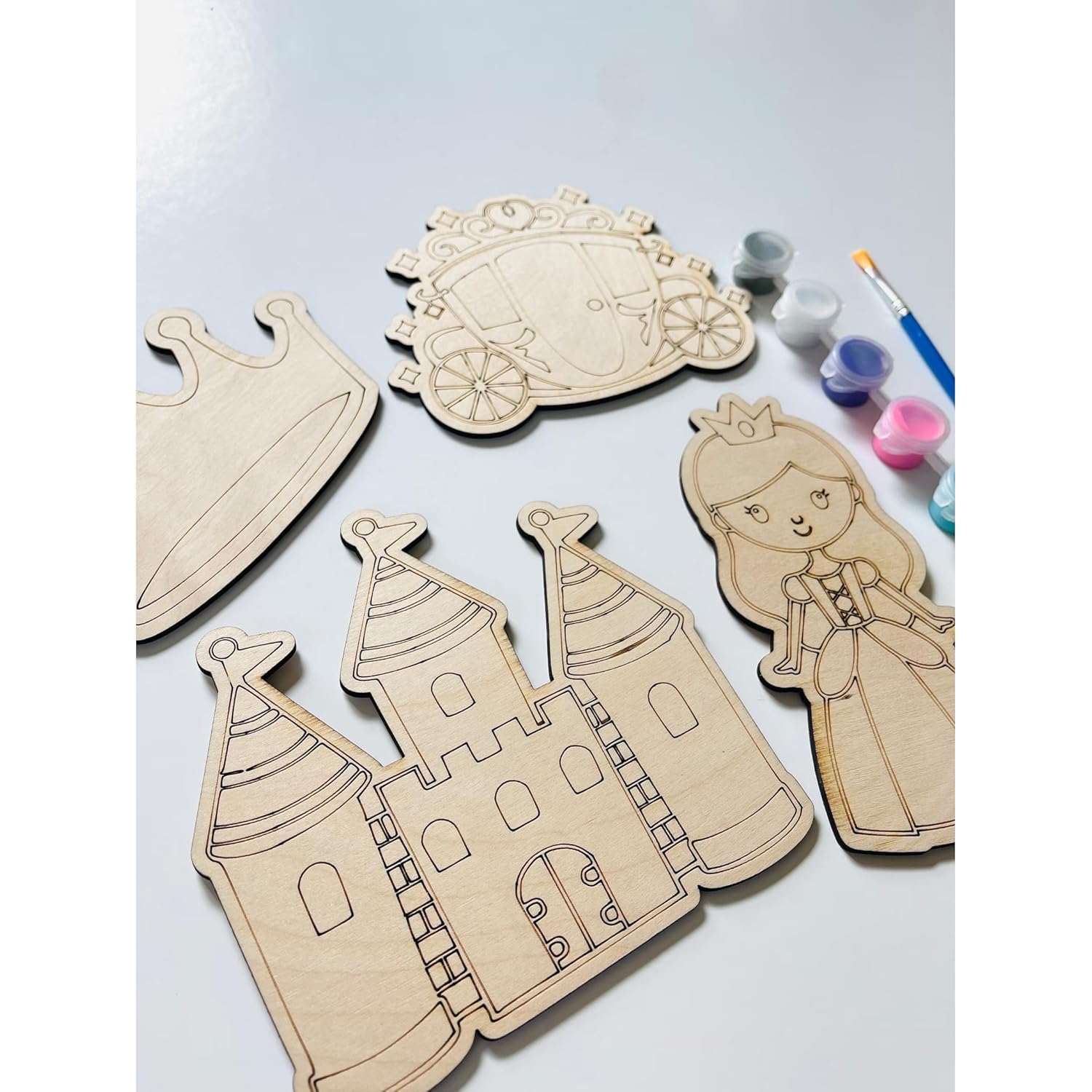 Wooden cutouts of a castle, princess, and carriage with paint supplies on a light blue background