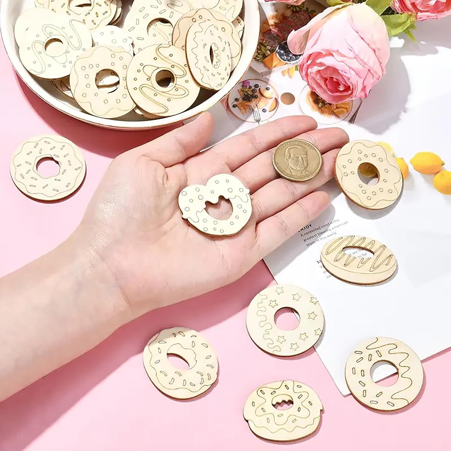 Hand holding a gold donut-shaped coin with more donut-shaped coins on a pink surface.