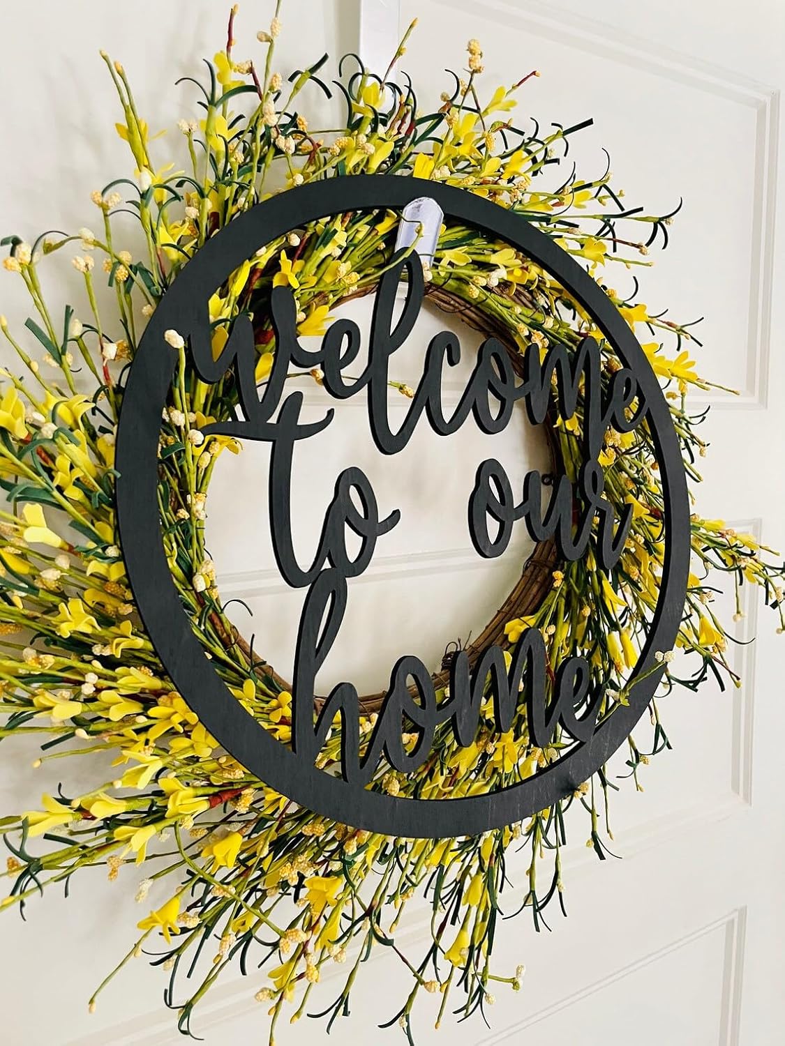 Decorative wreath with yellow flowers and 'Welcome to our home' text on a white door.