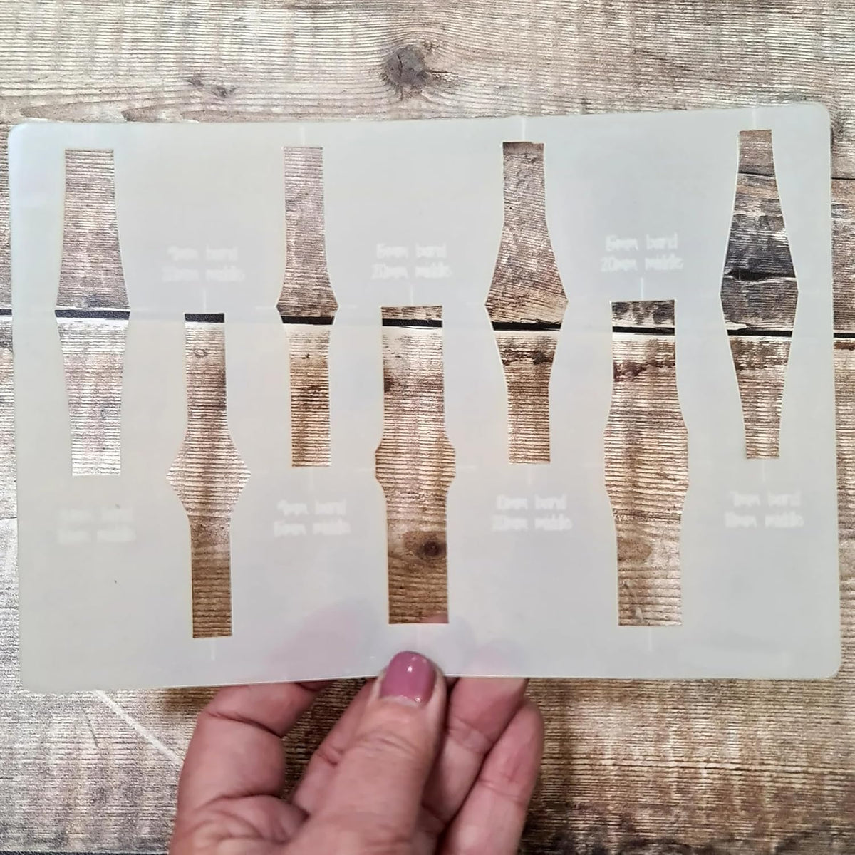 Hand holding a set of clear plastic templates on a wooden surface