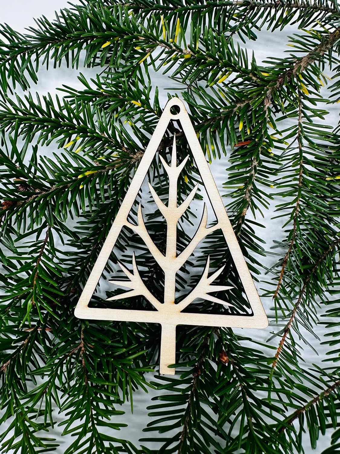 Decorative triangle ornament with tree branch design on a green pine branch background