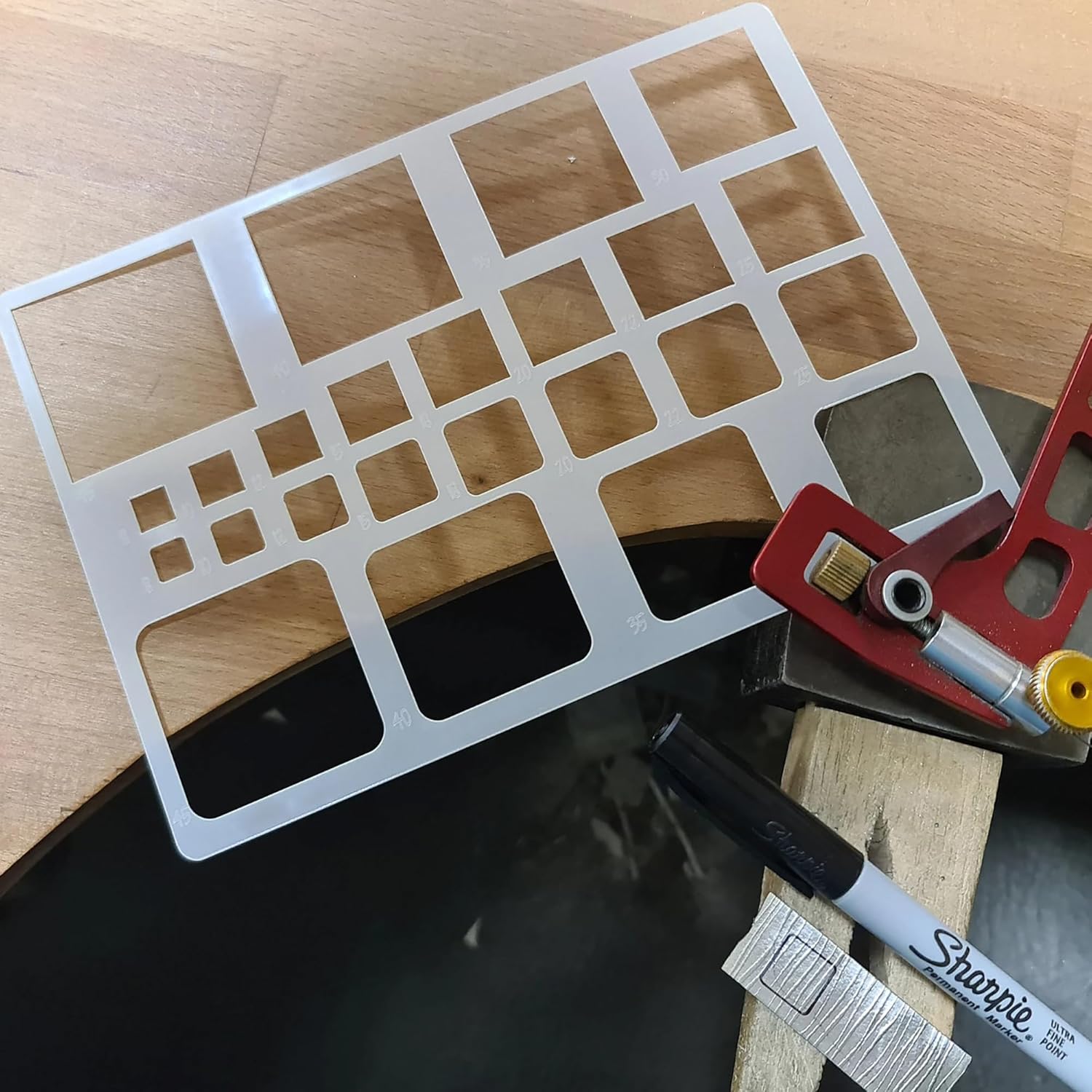 Metal template with cut-out shapes on a wooden surface with a Sharpie marker.