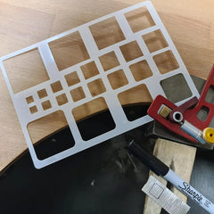 Metal template with cut-out shapes on a wooden surface with a Sharpie marker.
