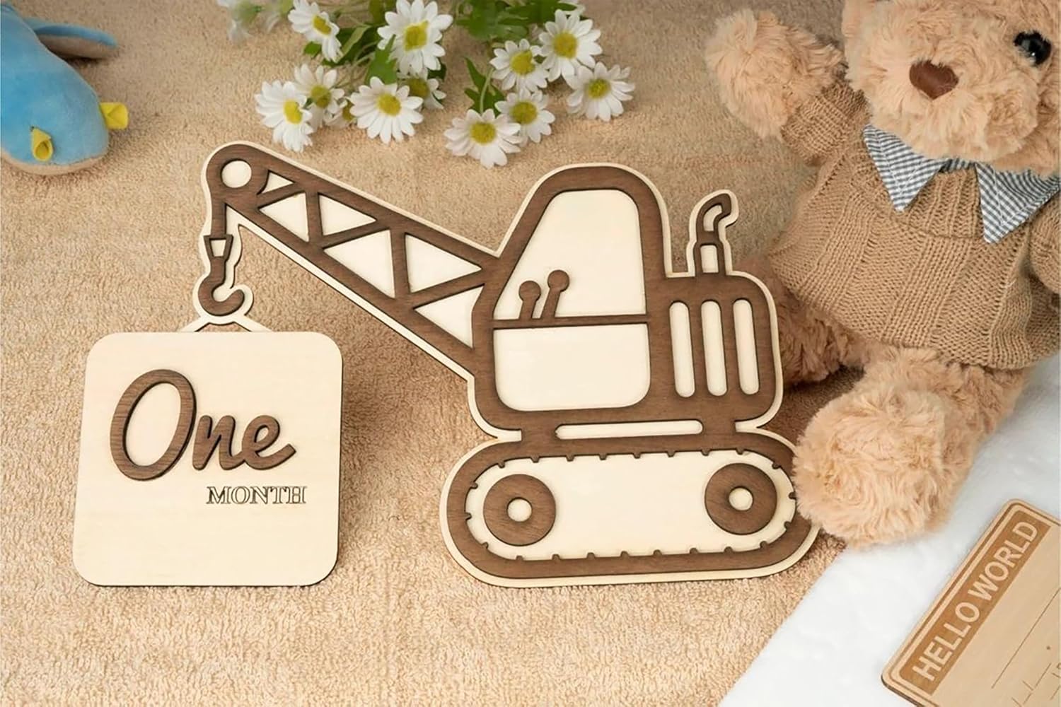 Wooden construction vehicle milestone with 'One Month' tag, teddy bear, and flowers on a textured surface.