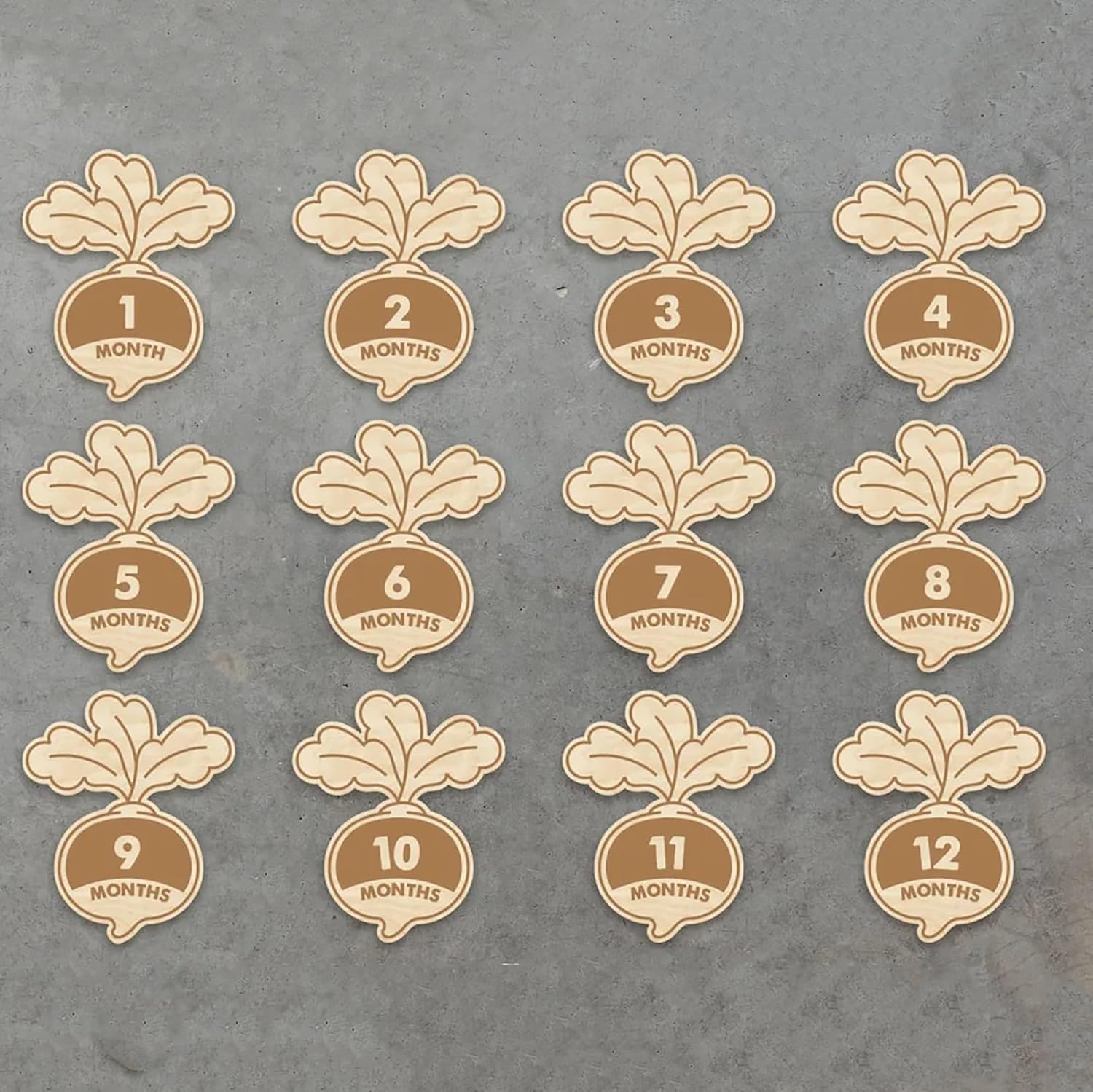 Set of wooden baby milestone cards with floral designs and month labels on a gray background.