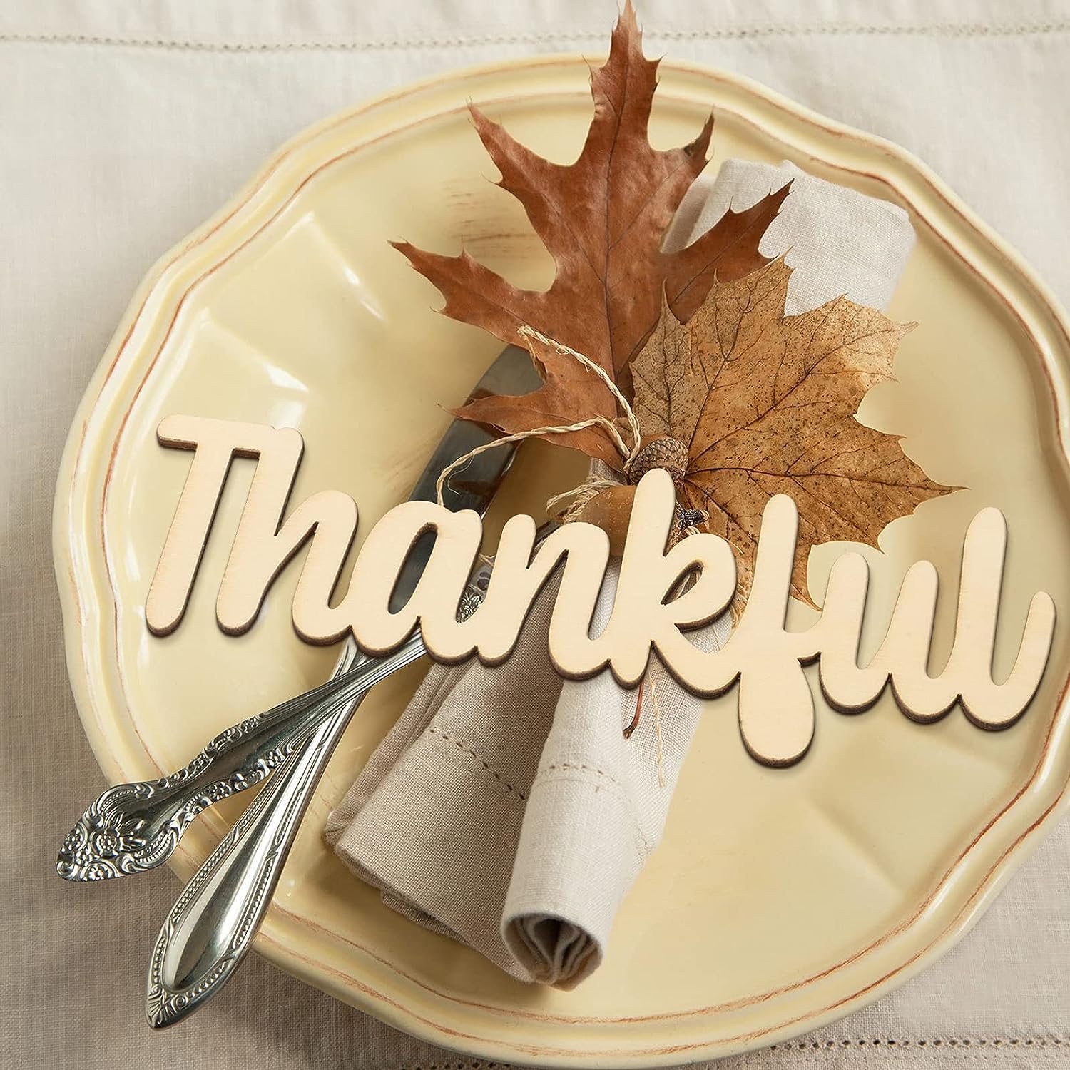 Decorative plate with 'Thankful' text, leaves, and silverware on a neutral background
