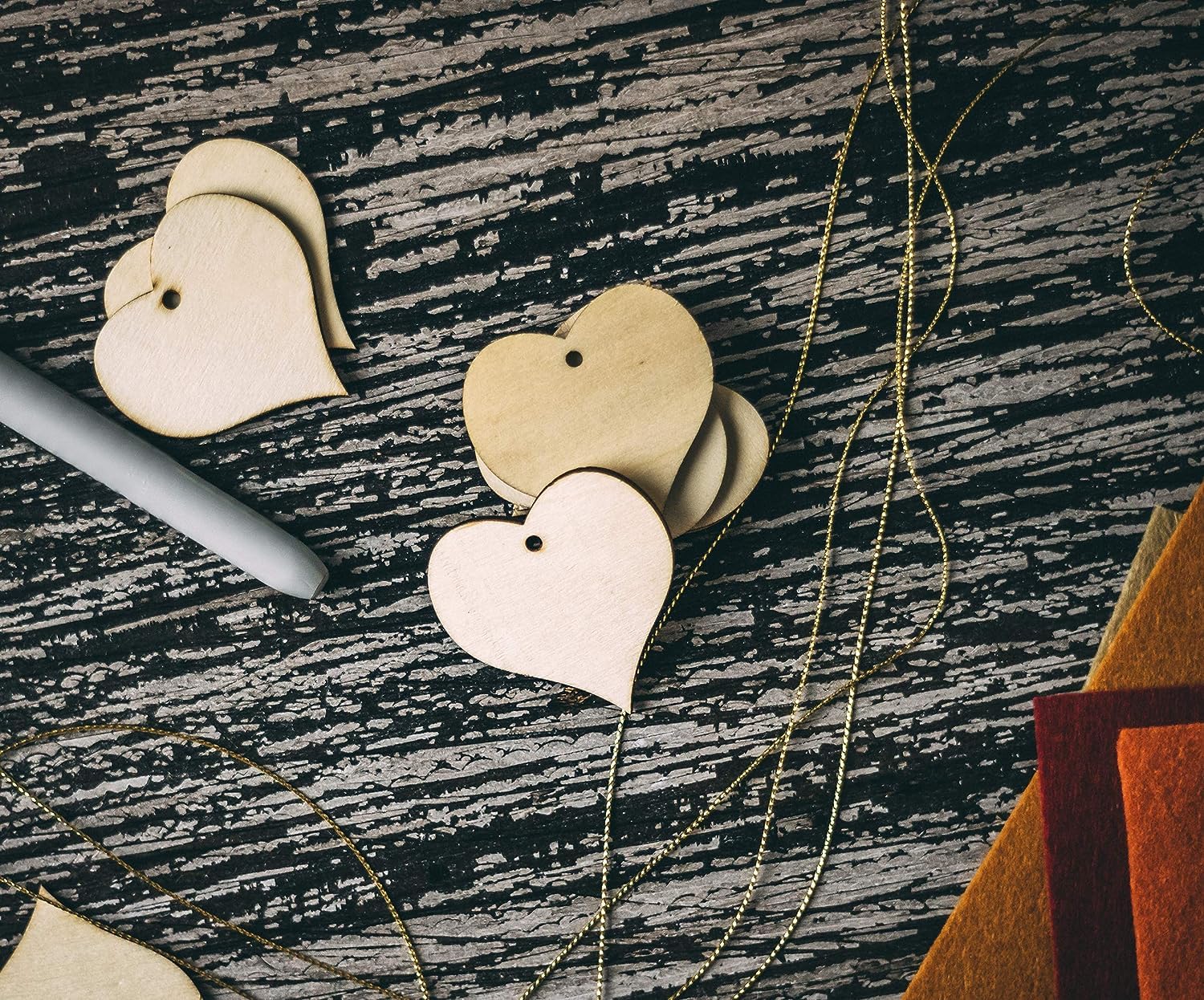 Heart-shaped wooden earrings on a textured surface with a pen and book in the background.
