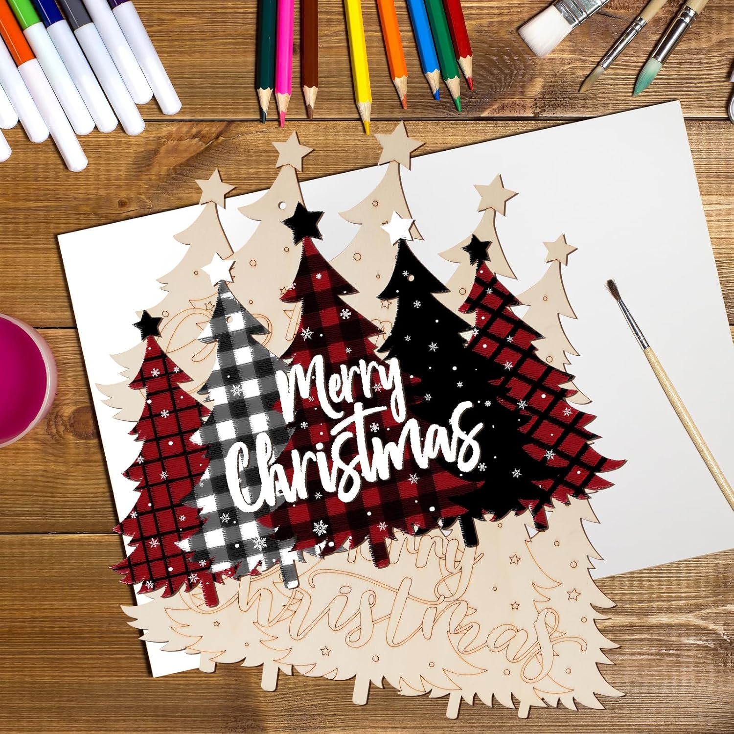 Christmas-themed cutout design with 'Merry Christmas' text on a wooden surface with coloring supplies.
