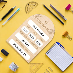 Wooden plaque with 'My First Day of' text on a yellow background with school supplies.